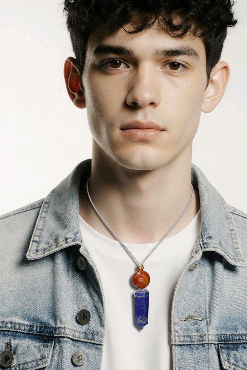 May include: A necklace with a pendant featuring a red-orange sphere above a blue crystal. The pendant hangs from a thin, gray cord. The person in the image is wearing a denim jacket and a white t-shirt.